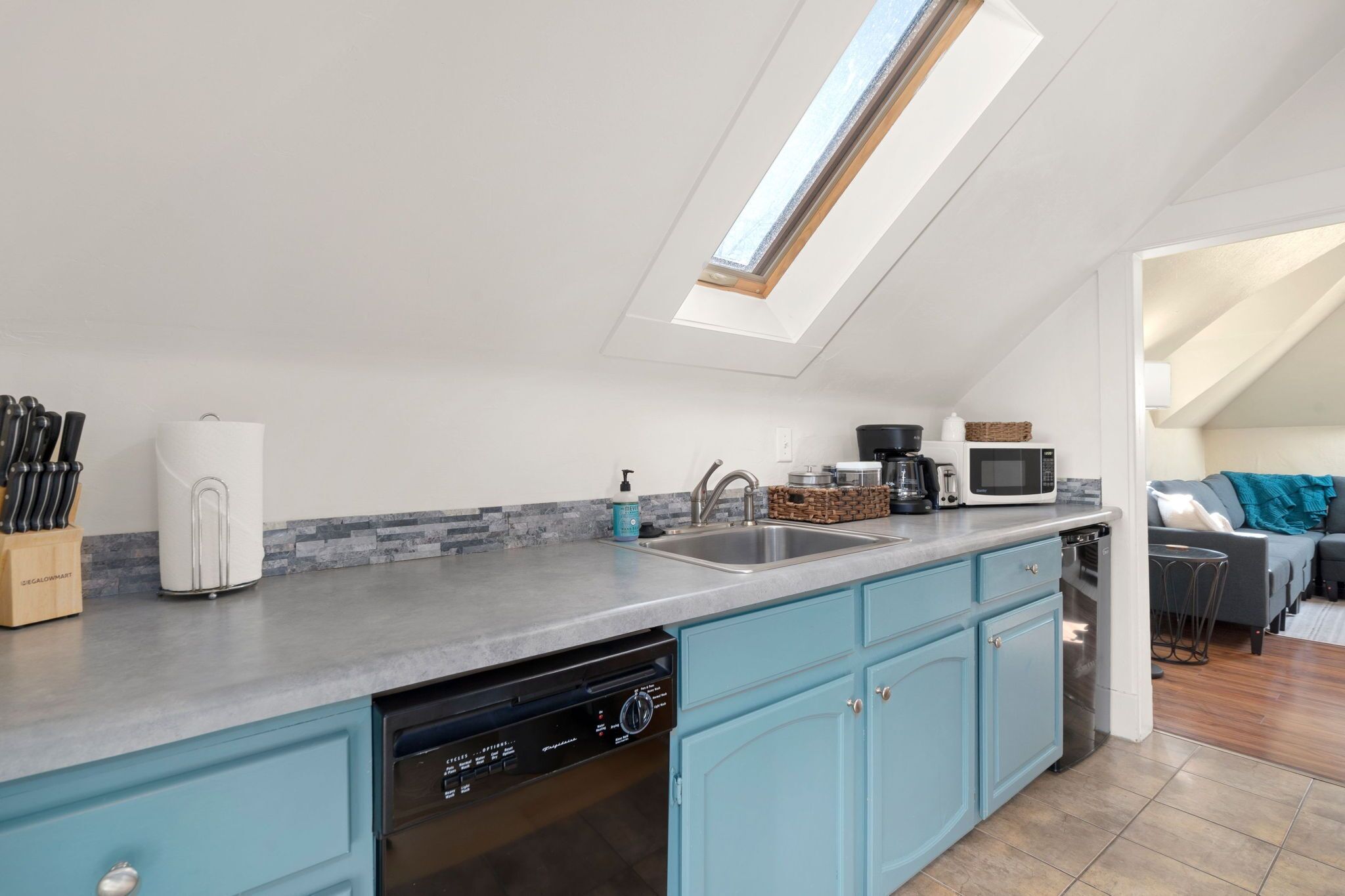 A modern kitchen with a skylight, built-in dishwasher, and a grey countertop.