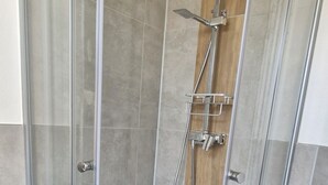 A glass-enclosed shower stall with a showerhead, handheld shower, and a wall-mounted faucet. - Vacation apartment Schwalbennest (Großschirma)