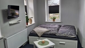 A small, neatly arranged bedroom with a bed, a TV mounted on the wall, a window with a plant, and a radiator. - Vacation apartment Schwalbennest (Großschirma)