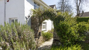 A white building with a stone archway covered in ivy, a stone pathway, and various green plants. - Sparnal Stitch nestled within the trees, just moments from sandy beaches (Rock)