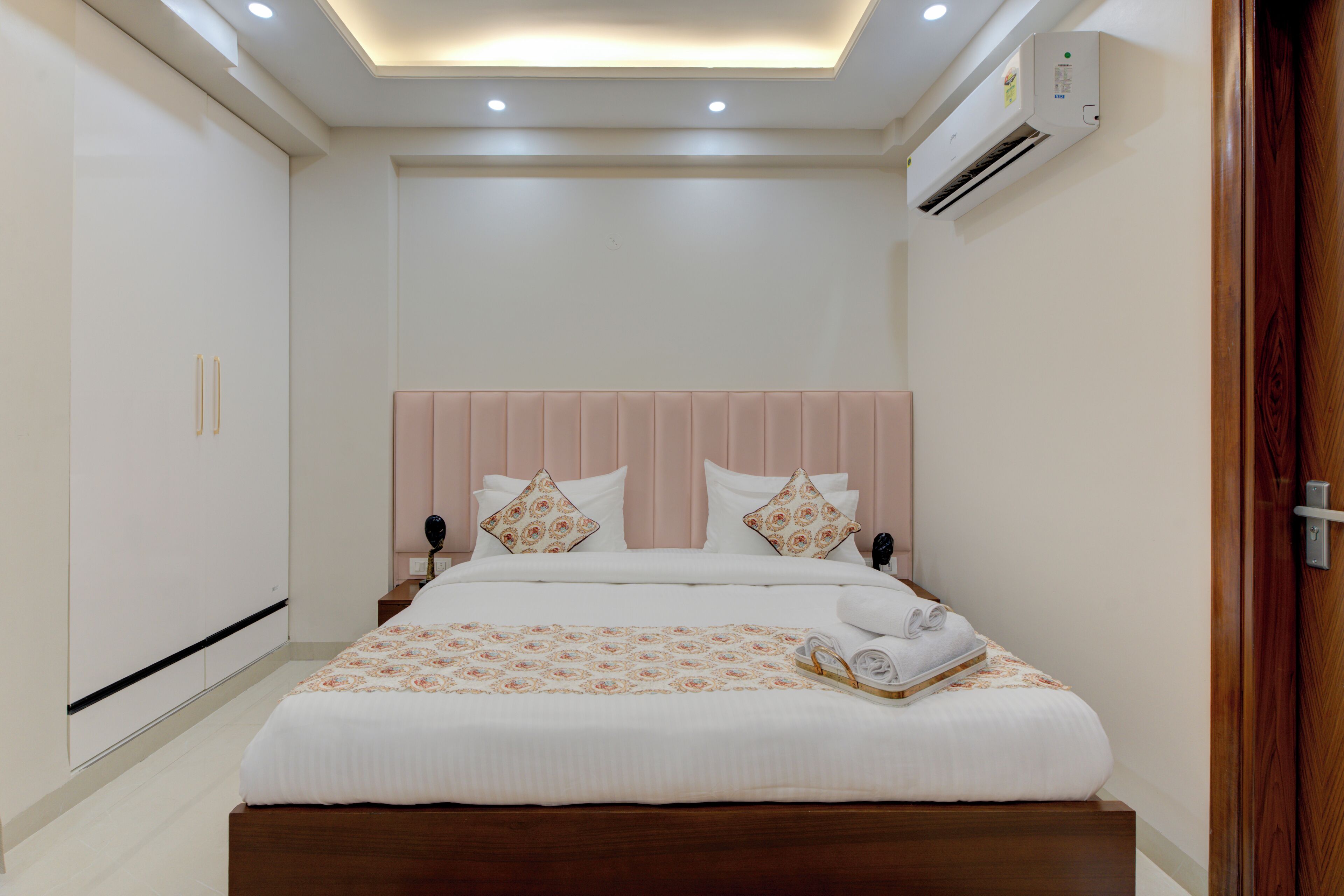 A neatly arranged hotel room with a large bed, a wooden headboard, and a built-in air conditioning unit.