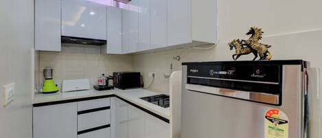 A modern kitchen with white cabinets, a black microwave, and a refrigerator with a decorative horse figure.