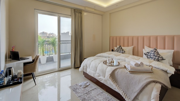 Een moderne hotelkamer met een groot bed, een bureau met een laptop, een koffiezetapparaat en een dienblad met glazen en handdoeken.