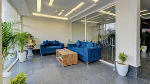 Een moderne lobby met twee blauwe banken, een houten salontafel en potplanten.