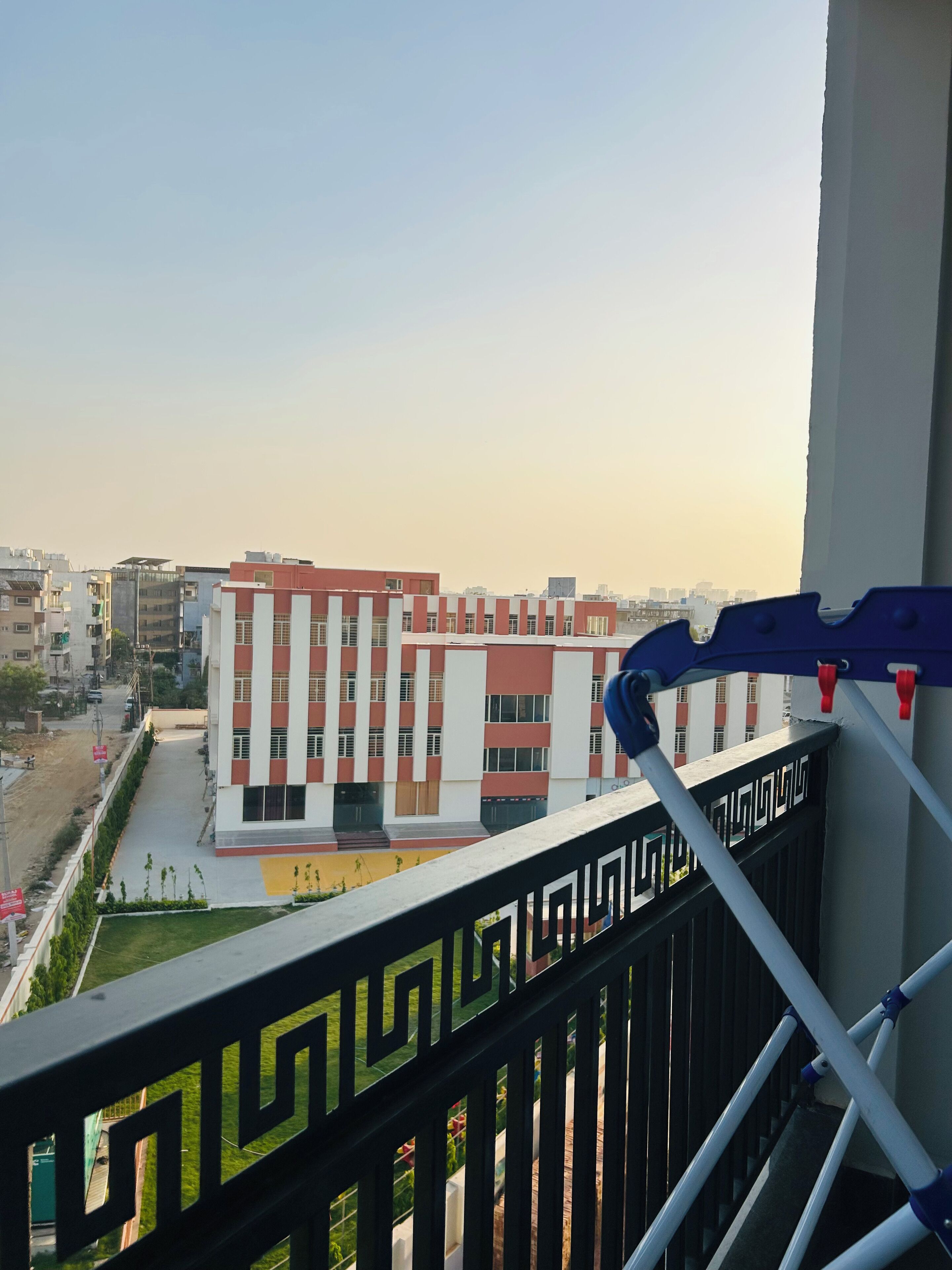 A balcony with a geometric railing, overlooking a modern building with red and white panels and a green lawn.
