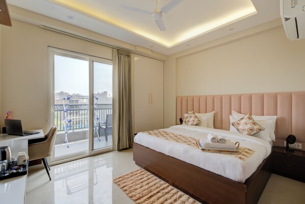 A hotel room with a bed, a desk, a laptop, and a view of the city through the window. - The Lodgers 1 BHK Apartments Sector 52 (Gurugram)