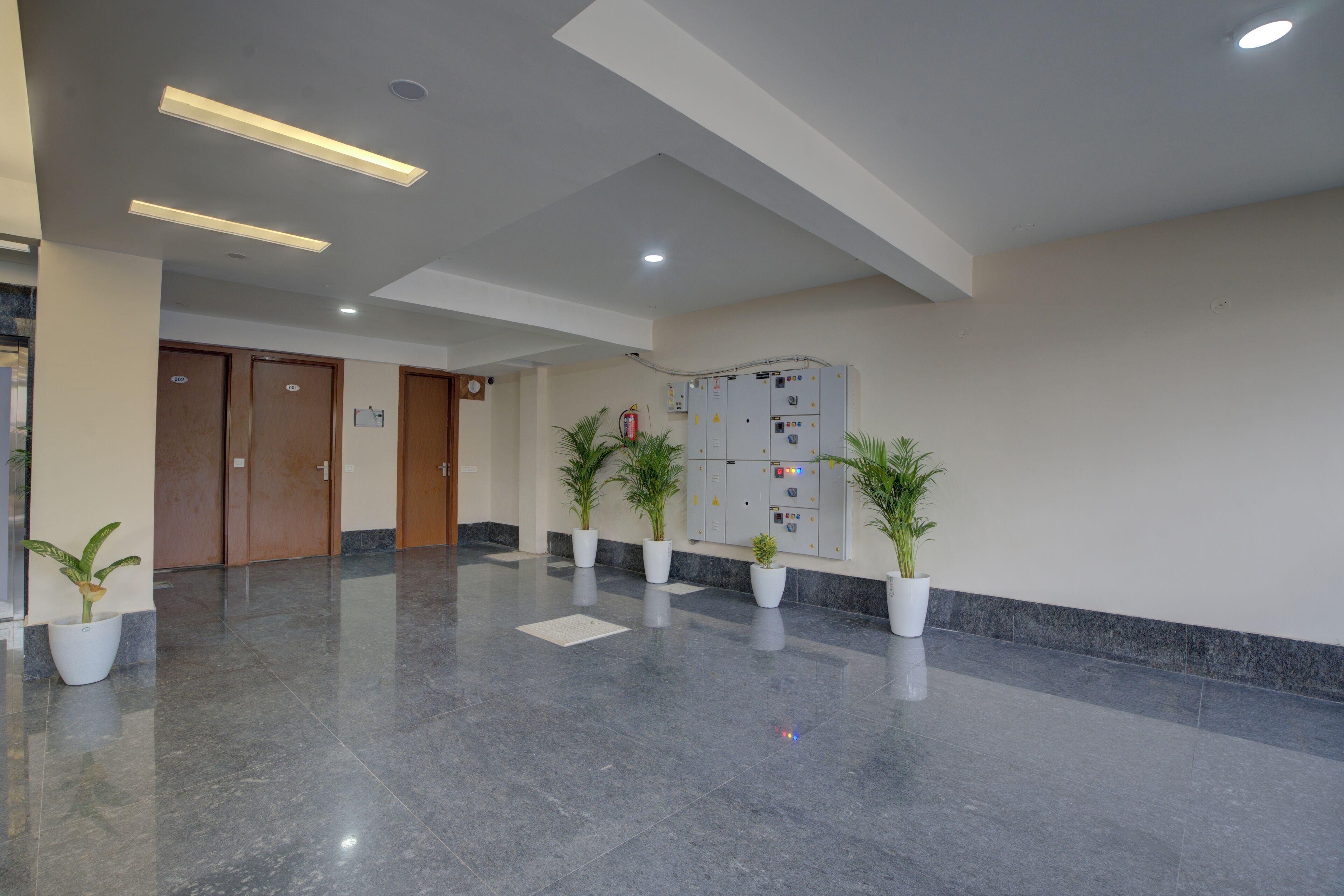 A spacious lobby with a polished marble floor, wooden doors, and potted plants.