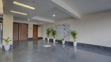 A spacious lobby with a polished marble floor, wooden doors, and potted plants.
