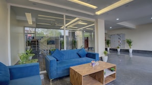 Een moderne lobby met een blauwe bank, een houten bijzettafeltje en potplanten.