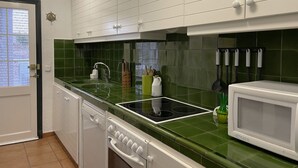 Een keuken met witte kastjes, een groen aanrecht, een fornuis en een magnetron.