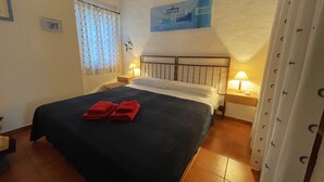 Een hotelkamer met een bed, twee bedlampjes, een raam met gordijnen, een wandklok en een schilderij.