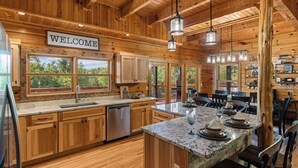 Cocina tipo cabaña de madera con un letrero que dice 'WELCOME', encimeras de granito y una zona de bar con botellas de vino.
