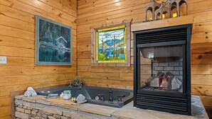 Interior de una cabaña de madera con chimenea de piedra, un lavabo de piedra y un cuadro que muestra una cabaña sobre un lago nevado.