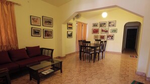A living room with a sofa, coffee table, and dining area with chairs. There are framed pictures on the walls. - Coorg Shell (Madikeri)