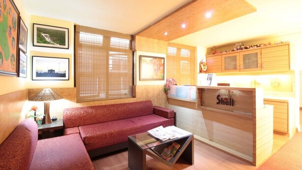 A hotel lobby with a red sofa, a reception desk, and framed pictures on the walls. - Coorg Shell (Madikeri)