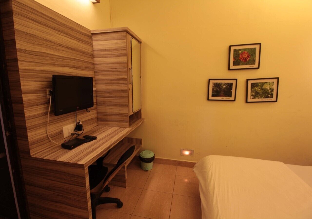 A bedroom with a wooden desk, a television, a bed, and three framed pictures on the wall.