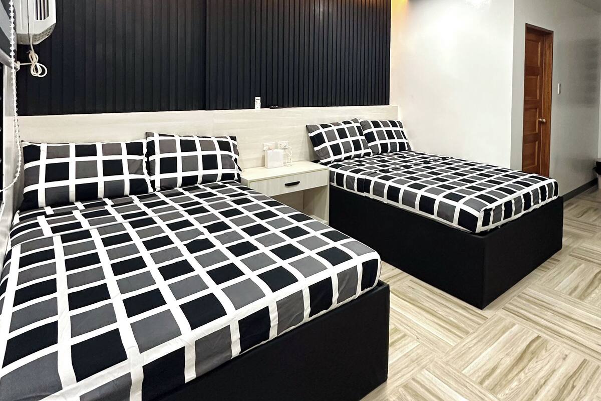 A modern bedroom with two beds, a wooden panel wall, and a ceiling light.