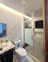 Un baño con tocador de mármol, inodoro y ducha con mampara de vidrio.
