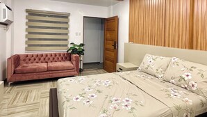 A bedroom with a bed, a sofa, a wooden panel wall, a ceiling light, and a door. - Casa Monica (Tuguegarao)