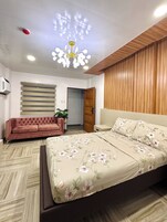 Un dormitorio con cama, sofá, pared de paneles de madera, luz de techo y puerta.