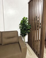 Una sala de estar con un sofá marrón, una planta en maceta y un separador de madera.
