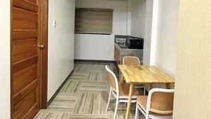 A compact kitchen with a microwave, a wooden table, and two wicker chairs. - Casa Monica (Tuguegarao)