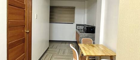A compact kitchen with a microwave, a wooden table, and two wicker chairs.
