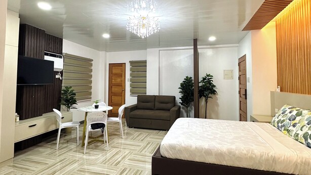 A modern bedroom with a large bed, a TV, a dining table with chairs, and a chandelier. - Casa Monica (Tuguegarao)