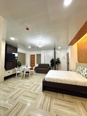 Een moderne slaapkamer met een groot bed, een televisie, een eettafel met stoelen en een kroonluchter.