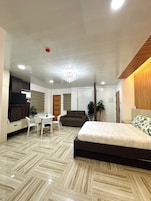 Un dormitorio moderno con una cama grande, televisión, mesa de comedor con sillas y una araña.
