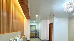 A modern hotel room with a large bed, a wooden slat wall, a small kitchenette, and a chandelier. - Casa Monica (Tuguegarao)