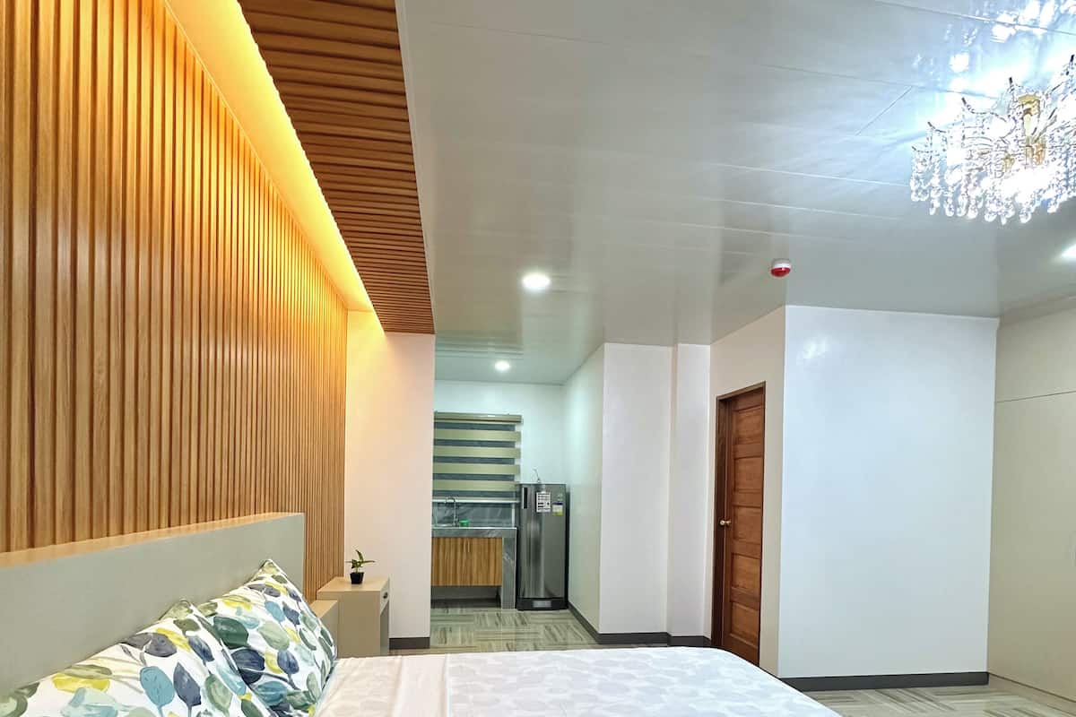 A modern hotel room with a large bed, a wooden slat wall, a small kitchenette, and a chandelier.