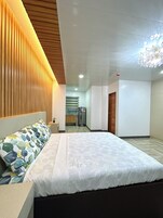 Una habitación de hotel moderna con una cama grande, un revestimiento de pared de listones de madera, una pequeña kitchenette y un candelabro.