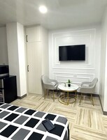 Una habitación de hotel con una cama, un televisor montado en la pared, dos sillas alrededor de una mesita y un armario.