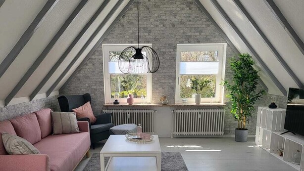 A modern loft bedroom with a sloped ceiling, exposed brick walls, and large windows. - Quiet and centrally located apartment (approx. 80m/2) Friedeburg "The gateway to the North Sea" (Friedeburg)