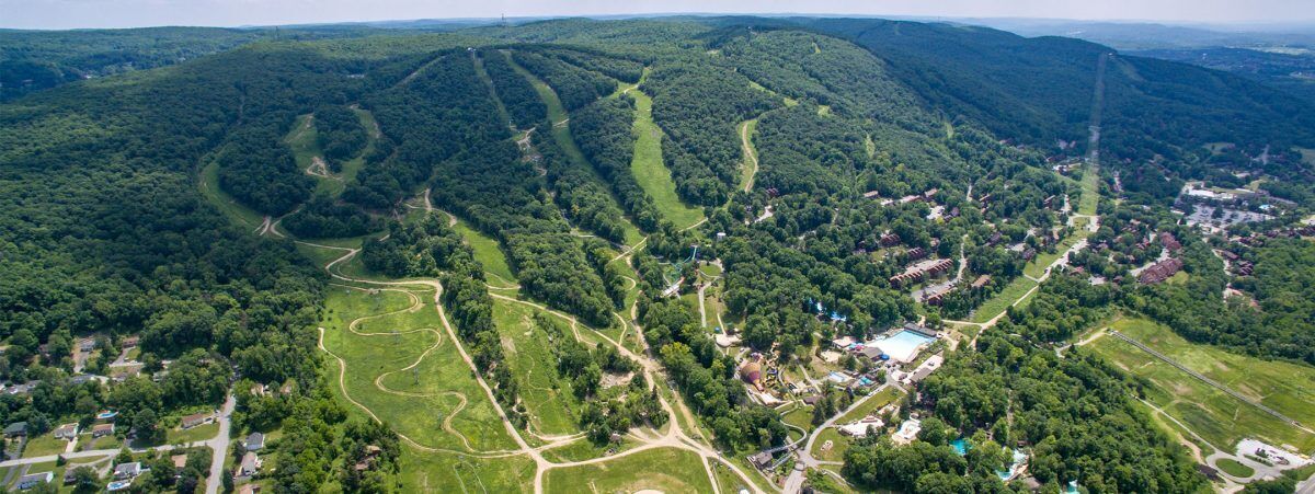 Vista aérea de una zona montañosa con senderos sinuosos, un pequeño asentamiento y una gran masa de agua.