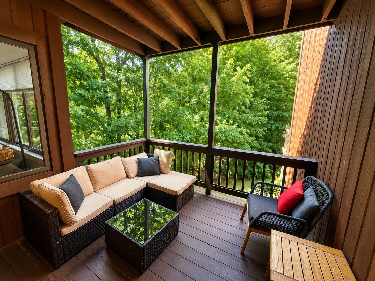 Ein überdachter Außenbereich mit einer Couch und Sesseln, einem Couchtisch und Blick auf einen Wald.