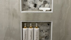 A bathroom with a marble backsplash and three bottles labeled "Shampoo," "Conditioner," and "Body Wash."