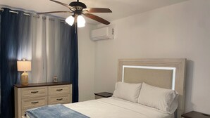 A bedroom with a bed, a nightstand, a lamp, a ceiling fan, and a window with curtains.