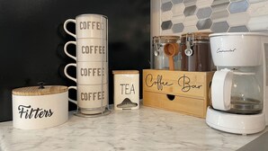 A kitchen counter with coffee-related items including a stack of coffee mugs, a coffee bar, a coffee maker, and a tea container.