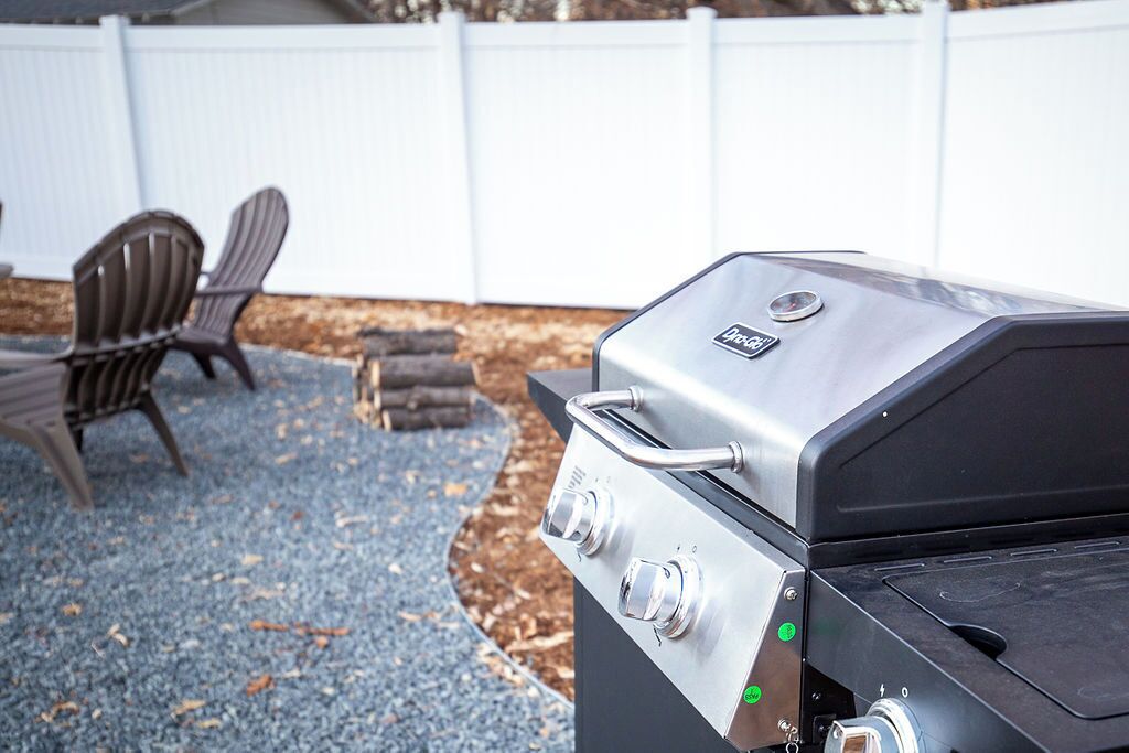 Un barbecue avec un panneau de commande, une chaise et, au fond, une clôture blanche.