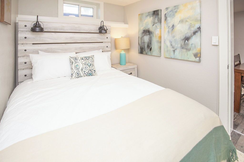 A bedroom with a wooden headboard, white bedding, a teal lamp, and abstract art on the wall.