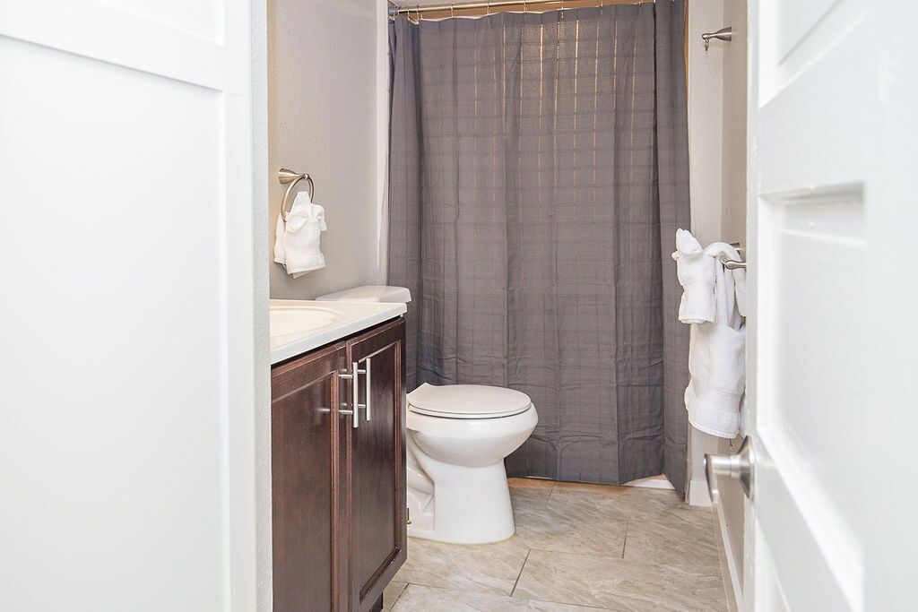 A bathroom with a toilet, a sink, a shower curtain, and a towel rack.