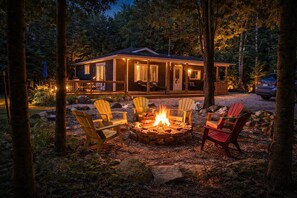 A cabin with a fire pit and Adirondack chairs in a forest setting. - Peninsula Perch: Water & Trails (Wiarton)
