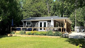 A two-story house with a deck, surrounded by a well-maintained lawn and garden. - Peninsula Perch: Water & Trails (Wiarton)