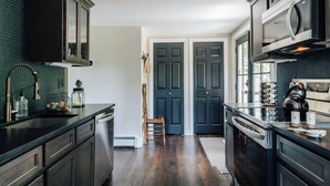 Une cuisine moderne avec des meubles de couleur sombre, des appareils en acier inoxydable et une chaise en bois.