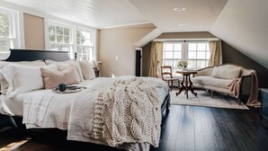 Une chambre avec un grand lit, une chaise, une petite table et une fenêtre.