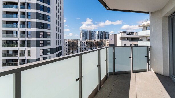 Un appartement moderne doté d’un balcon, de grandes fenêtres et offrant une vue sur d’autres immeubles de grande hauteur.