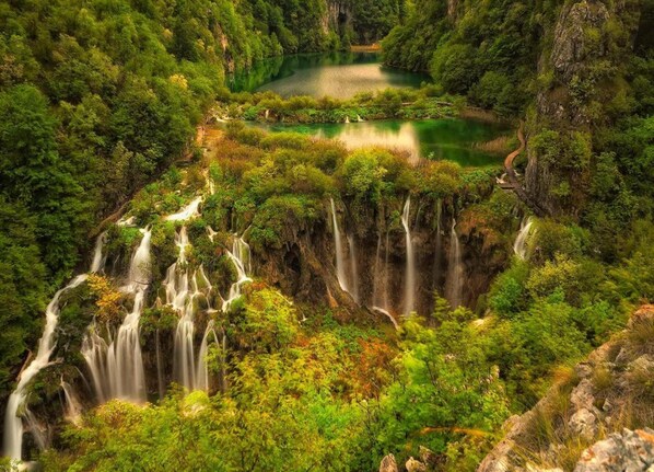 A lush, mountainous landscape with multiple waterfalls and a serene lake surrounded by dense greenery.