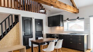A modern kitchen with black cabinets, a wooden dining table, and white chairs. - Gîte on a farm with animals, near Arromanche-les-bains, 2 km from the sea (Ryes)